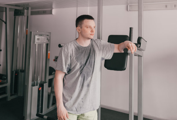 一个穿着湿t恤的疲惫运动员的肖像就站在模拟器旁边。图片下载