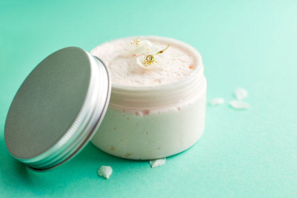 瓶白色护肤霜与新鲜的春天樱花。化妆品瓶。植物spa治疗娇嫩肌肤。青绿色的背景图片下载