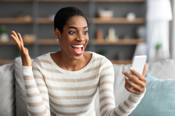 兴奋的非裔美国妇女看着智能手机，情绪上对好消息的反应图片下载