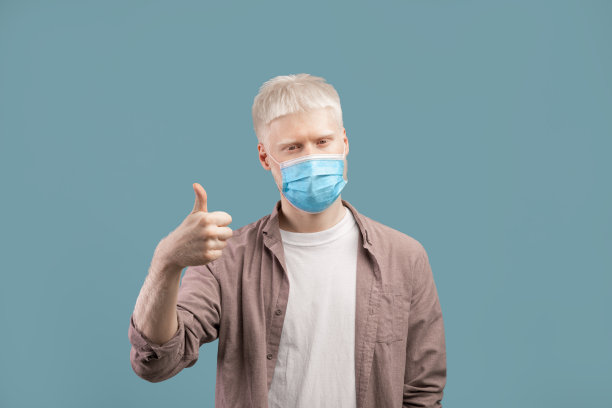 保持安全。白化人在医疗防护面具显示拇指在工作室背景图片下载
