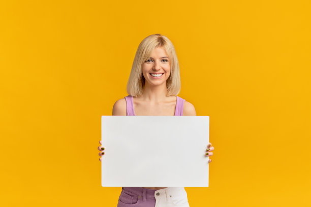广告的概念。兴奋的女人抱着空白板孤立在黄色工作室背景图片下载