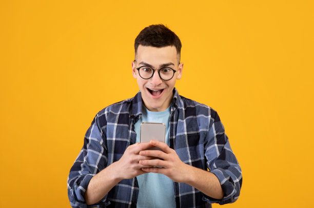 在橙色工作室背景下使用手机进行在线交流、工作或学习的时髦年轻人图片下载