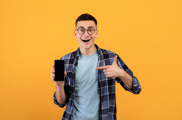 身着休闲装的千禧一代兴奋地指着橙色背景上的空白屏幕的智能手机，为你的应用留出空间图片下载