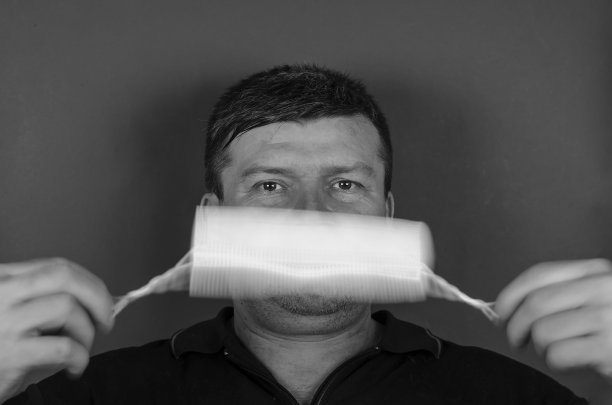 一名成年男性在自己面前旋转医用口罩的肖像。图片下载