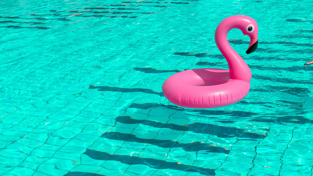 夏天的乐趣。粉红色的充气火烈鸟在游泳池的水为夏天的海滩背景。奢侈的生活方式。图片下载