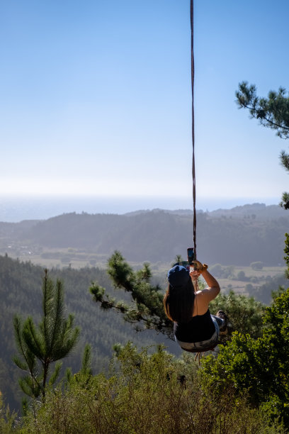 在智利森林垂直照片中，一名女子在山顶的户外秋千上图片下载