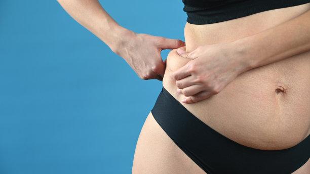 女人在内裤是站在一边，显示褶皱的腹部脂肪在蓝色的背景。减肥图片下载