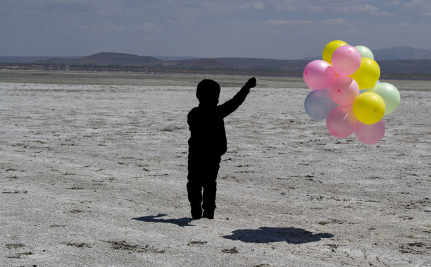 一个男孩带着彩色气球在海滩上散步的影子图片下载