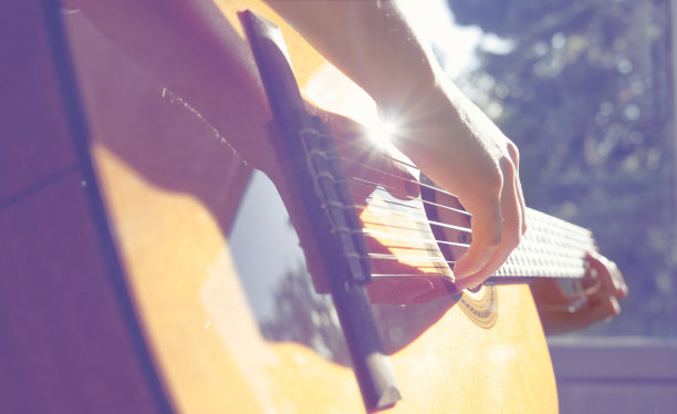 一个男人在外面弹吉他的特写，阳光反射在木头上图片下载