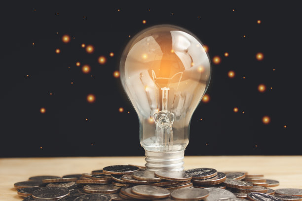 温暖的灯泡和一堆硬币与拷贝空间上的黑色散景黑底。图片下载
