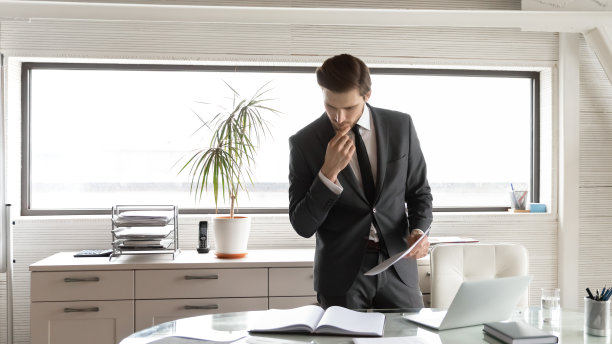 深思熟虑的商人在办公室触摸下巴，查看财务文件图片下载