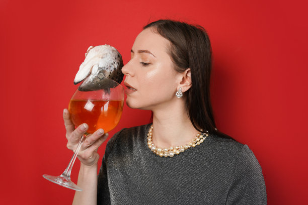 美丽的年轻女子，戴着珠宝，喝着葡萄酒杯，红色背景上有新鲜的鱼头图片下载