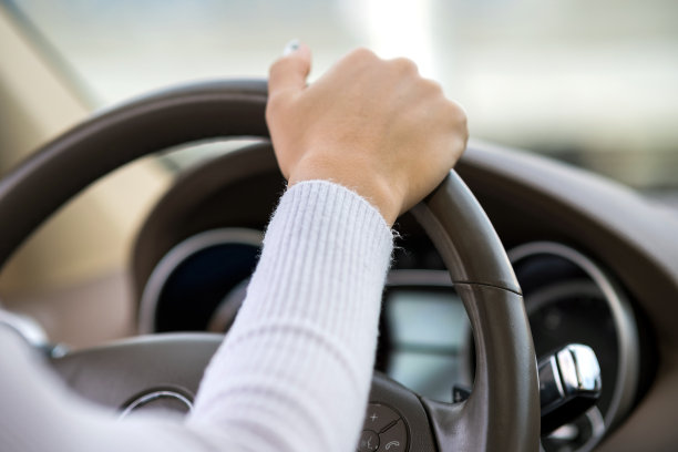 在阳光明媚的日子里，女人手持方向盘在城市街道上开车。图片下载