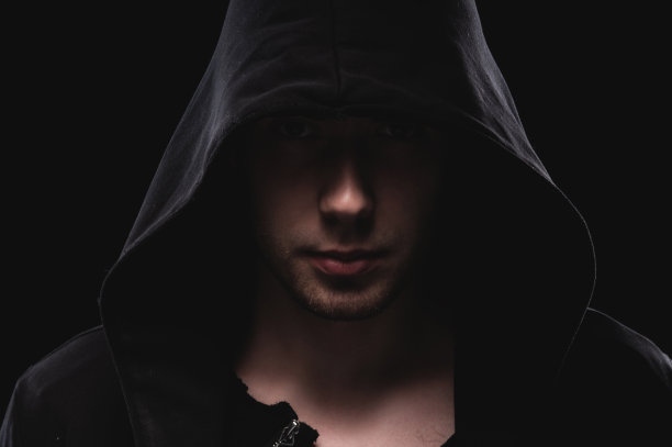 一个戴兜帽的人的剪影或一个恶棍在一个黑色的背景。黄昏时分一个罪犯的脸图片下载