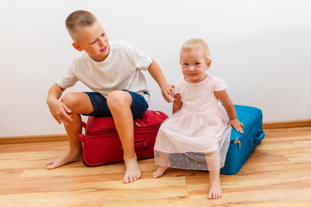 男孩和女孩坐在房间里的大行李箱上图片下载