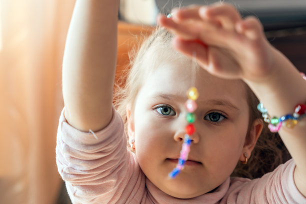 一个小女孩正在做针线活，她用自己的双手做珠宝，用一根线串起五颜六色的珠子图片下载
