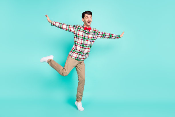 男子跳舞的照片手翅膀飞机姿势站一条腿穿格子衬衫蝴蝶结裤子孤立的蓝色背景图片下载