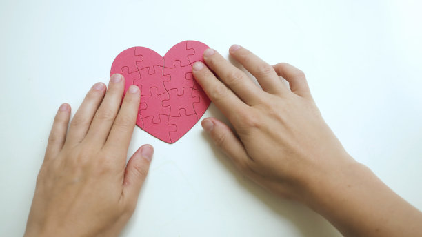 Top view on女人的双手触摸红色的心形拼图从纸块拼图在白色的桌子背景图片下载