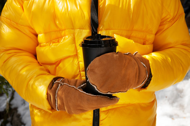 在冬天的hwaon森林里，一名穿着黄色羽绒服、戴着手套的妇女手里拿着一杯热咖啡或茶图片下载