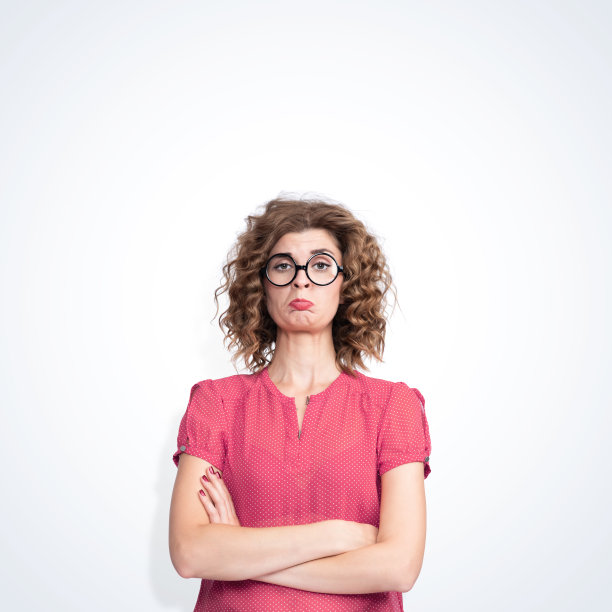 年轻漂亮的女孩戴着圆眼镜，穿着带有圆点的裙子，在浅色的背景下，她的脸上露出了强烈的怨恨。图片下载