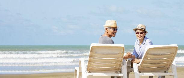 亚洲老夫妇戴着太阳帽坐在沙滩椅上图片下载