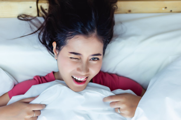 快乐的年轻女人醒来在床上的新鲜美丽的女孩有一个美好的一天与顶视图微笑的亚洲女性醒来后睡得很好她醒来舒适的床在舒适的卧室毯子图片下载