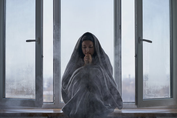 寒冷的冬天的天气。窗台上，一个裹着毯子的女人冻得发抖。寒冷的空气从开着的窗户冲了进来。在寒冷的冬天通风房屋图片下载