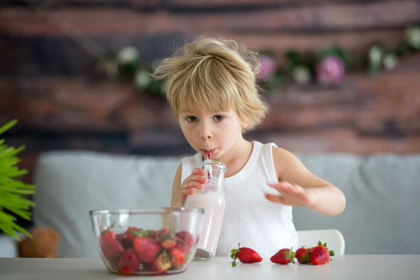 可爱的蹒跚学步的孩子，金发男孩，喝着冰沙和吃着草莓图片下载