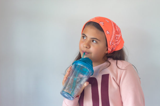 戴着围巾的女孩在一个蓝色保温瓶里喝水，白色的背景图片下载