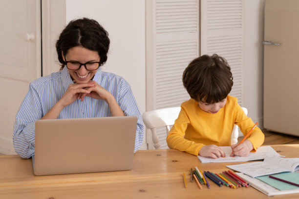 新冠肺炎一级防范禁闭期间，千禧一代商界女性在家用笔记本电脑工作，带着年幼的儿子坐在办公桌前图片下载