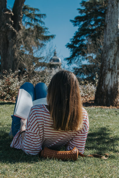 一个女孩坐在草地上看书的垂直镜头图片下载