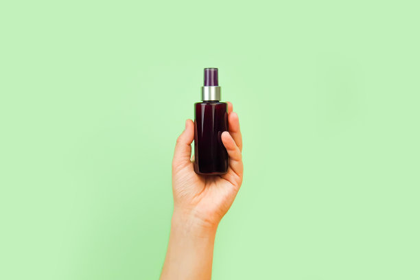 男性的手拿着没有品牌的棕色塑料喷雾器瓶在柔和的绿色背景上。化妆品瓶容器，用于药品或化妆品的商标。天然有机温泉身体喷雾。模型图片下载