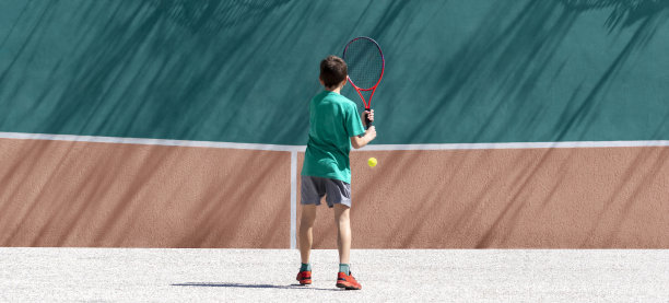 网球小男孩独自打网球，练习击球技术，靠墙训练。儿童户外运动、游戏和休闲活动。后视图，宽横幅，复制空间图片下载