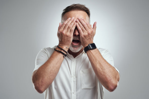 在灰色背景下，一个成年男子蒙着眼睛，看起来很震惊图片下载