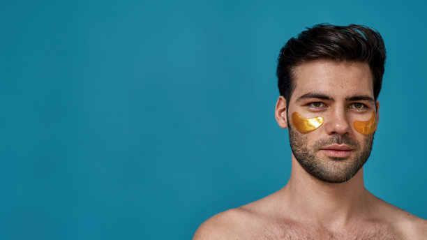工作室肖像的黑发白种人与金色凝胶下眼罩看向别处，摆出孤立的蓝色背景图片下载