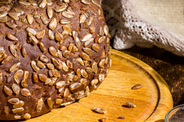 静物——黑面包配葵花籽，亚麻餐巾放在木板上，木质背景，强光，照片低调。图片下载