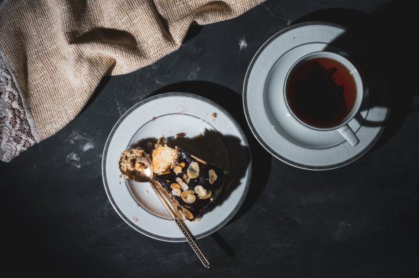 静物层次的自制海绵蛋糕和一杯红茶在一个白色的盘子，和亚麻餐巾，黑色的背景，强光，照片在一个低的关键。图片下载