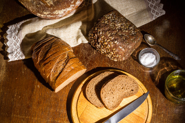 静物-无酵母荞麦面包，各种黑面包，橄榄油和粗盐在玻璃罐里，一把刀，和亚麻餐巾在木板上，一个木制的背景，硬光，一张低调的照片。图片下载