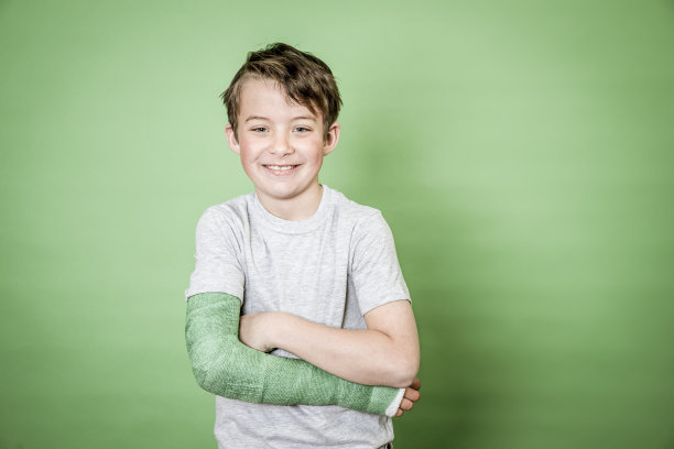 酷年轻的学生与骨折的手臂和绿色石膏站在前面的绿色背景图片下载