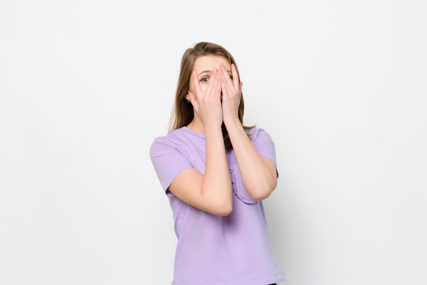 担心，害怕的年轻女子看着手指之间，孤立在白色的背景。一半长度的肖像图片下载