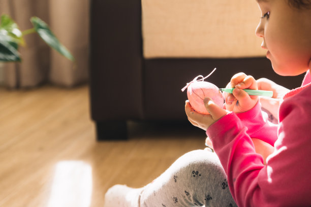 侧面照片上的女孩穿着粉红色的衣服坐在客厅的地板上画着复活节彩蛋图片下载