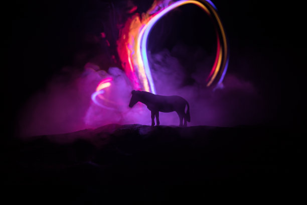 晚上在沙漠里奔跑的骏马。一个马的剪影微型站在雾蒙蒙的夜晚。创意桌子装饰与彩色背光与雾。有选择性的重点图片下载