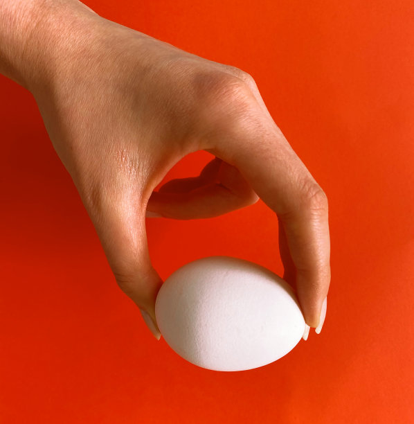 女人手上有白色的鸡蛋和橙色的背景图片下载