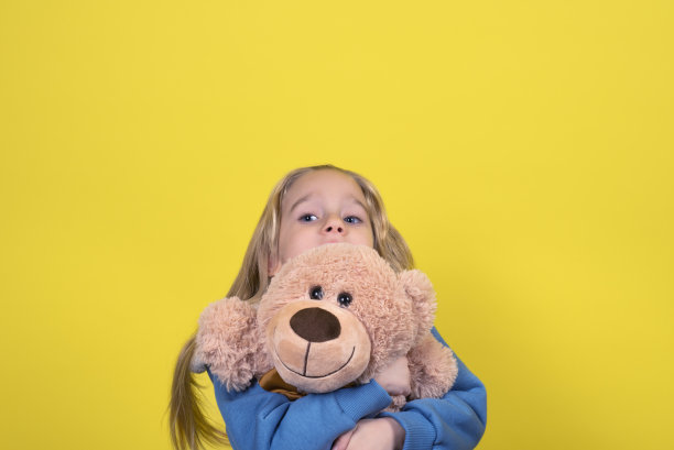 金发小女孩拿着玩具泰迪熊。穿着现代服装，留着长发的小女孩在玩泰迪熊图片下载