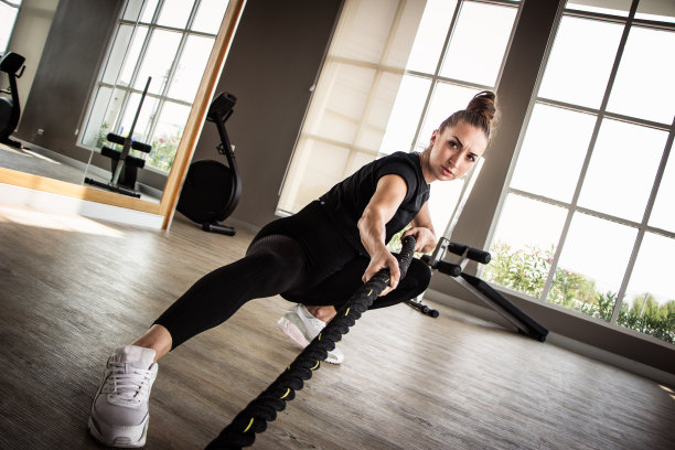 美丽的白种人女子在健身房里锻炼有背景的健身设备。运动女性在体育馆里用格斗绳练习图片下载