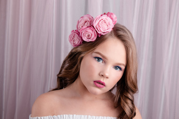 粉色丝绸背景上，头发戴着粉色玫瑰的少女。卷发中的鲜花。时尚照片。春季或夏季鲜花盛开图片下载