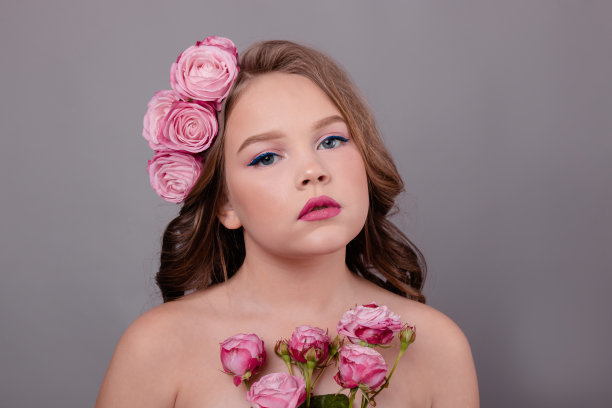 黑发少女与粉红色玫瑰在她的头发在灰色背景。头上卷着的花。时尚的照片图片下载