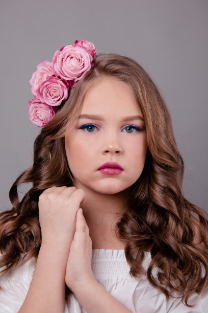 黑发少女与粉红色玫瑰在她的头发在灰色背景。头上卷着的花。时尚的照片图片下载