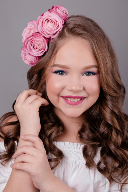 黑发少女与粉红色玫瑰在她的头发在灰色背景。头上卷着的花。时尚的照片图片下载