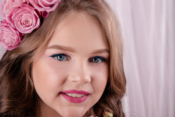 粉色丝绸背景上，头发戴着粉色玫瑰的少女。卷发中的鲜花。时尚照片。春季或夏季鲜花盛开图片下载